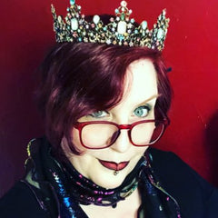 An image of Deven Rue looking very goth from the neck up. She has red lipstick purple hair and a fabulous crown on her head.